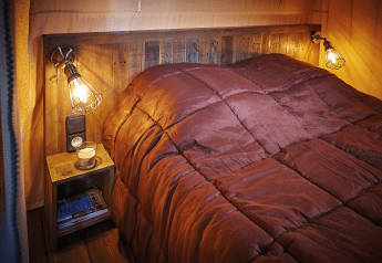 Dormitorio acogedor con edredón marrón, cabecero de madera y lámparas en Lodge op palen Confort 46m², Francia.