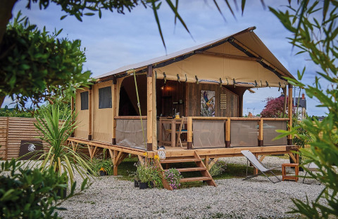 Safari-Zelt On stilts Lodge Confort mit Holzterrasse und Lounge-Stühlen, umgeben von Pflanzen und Kies.
