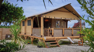 On stilts Lodge Confort safari tent with wooden deck, lounge chairs, and greenery under a partly cloudy sky.
