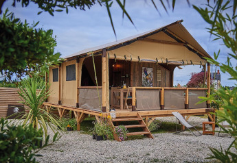 On stilts Lodge Confort safari tent with wooden deck, lounge chairs, and greenery under a partly cloudy sky.