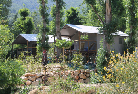 Tienda safari sobre pilotes en Flower Camping La Rivière en Francia, rodeada de árboles y vegetación.
