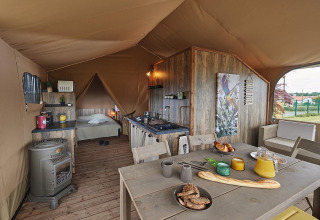 Interior de una tienda safari con suelo de madera, cocina y comedor en Flower Camping La Rivière, Francia.