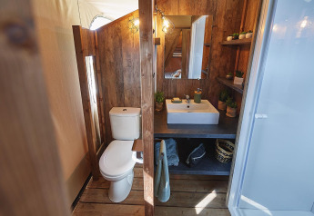 Bagno in una tenda safari con pannelli in legno, wc, lavandino e scaffali presso Flower Camping La Rivière.
