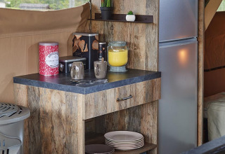 Pequeña cocina acogedora en tienda safari con acabado de madera, microondas, nevera y vajilla en Francia.