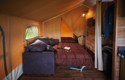 Vista interna di Lodge on stilts Confort con letto, divano e legno a Flower Camping La Rivière, Francia.
