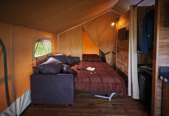 Binnenaanzicht van Lodge on stilts Confort met bed, bank en houtdecor bij Flower Camping La Rivière, Frankrijk.