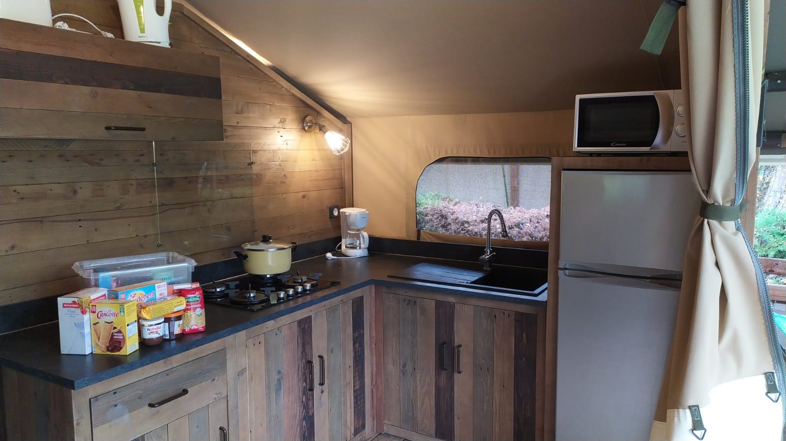 Keuken in Lodge on stilts Confort bij Flower Camping La Rivière in Frankrijk met houten kasten en apparatuur.
