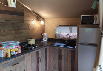 Keuken in Lodge on stilts Confort bij Flower Camping La Rivière in Frankrijk met houten kasten en apparatuur.