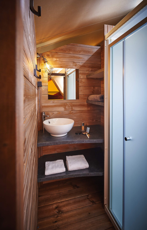 Badkamer met houten afwerking, waskom en douche in Lodge on stilts Confort, Flower Camping La Rivière, Frankrijk.
