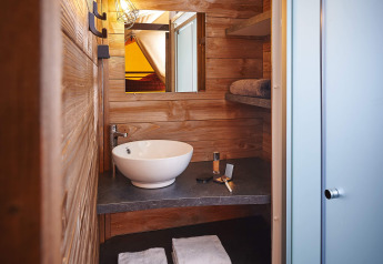 Badeværelse i træinteriør med rund vask, hylder, spejl og brusekabine på Lodge on stilts Confort i Frankrig.