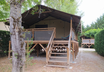 Vista frontale del Lodge on stilts Confort presso Flower Camping La Rivière, Francia, tra alberi e siepi.