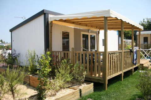 Glampingindkvartering med træveranda og overdækning, omgivet af grønne planter og velholdt have.