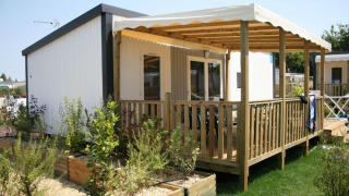 Glampingaccommodatie met houten veranda en overkapping, omgeven door een tuin met veel planten.