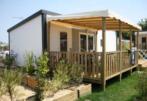 Glamping accommodation featuring a wooden deck with awning, surrounded by greenery and garden beds.