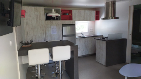 Modernes Glamping-Küche mit Bartresen, Hockern, Herd, Kühlschrank und Fenster im Hintergrund.