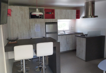 Moderne glampingkøkken med hjørnevindue, barstole, grå bordplader og indbyggede apparater.