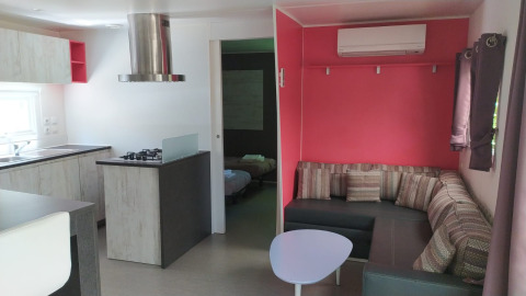 Alojamiento glamping moderno con cocina, sofá esquinero, aire acondicionado y dormitorio, interior luminoso.