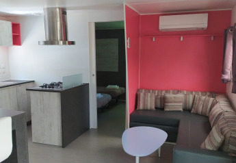 Alojamiento glamping moderno con cocina, sofá esquinero, aire acondicionado y dormitorio, interior luminoso.