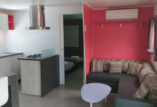 Hébergement glamping moderne avec cuisine, canapé d’angle, climatisation et chambre, intérieur lumineux.