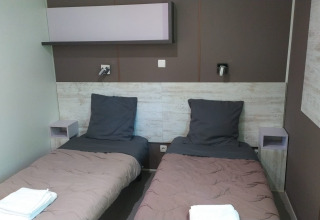 Modern glamping accommodation room with two single beds, gray bedding, and fresh towels on each bed.