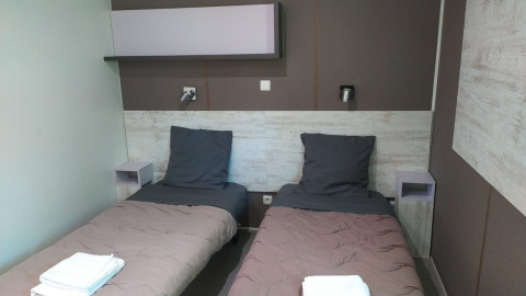 Sistemazione glamping moderna con due letti singoli, biancheria grigia e asciugamani puliti su ogni letto.