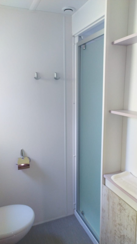 Moderne badkamer bij glamping, met douche, toilet en eenvoudig, licht interieur.