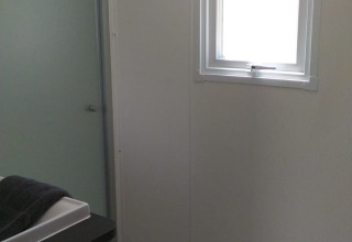 Badeværelse i et glampingophold med brusekabine, lille vindue, to knager og moderne vask.