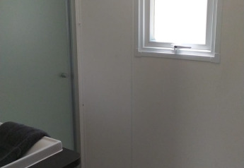 Badeværelse i et glampingophold med brusekabine, lille vindue, to knager og moderne vask.