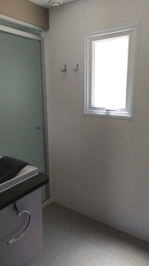 Badeværelse i et glampingophold med brusekabine, lille vindue, to knager og moderne vask.