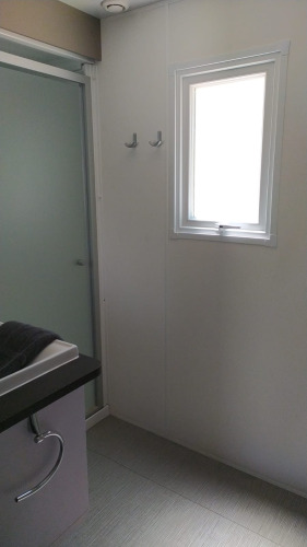 Salle de bain dans un logement de glamping avec douche, petite fenêtre, crochets et lavabo moderne.