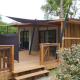 Foto af et glamping-opholdssted med træterrasse, solsejl og moderne udendørs siddeplads midt i naturen.