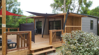 Foto van een glamping-accommodatie met houten terras, schaduwdoeken en stijlvolle buitenset in de natuur.