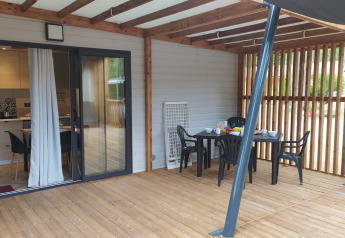 Veranda coperta in legno con tavolo da pranzo e sedie davanti a un alloggio glamping con cucina a vista.