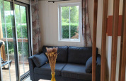 Gezellige zithoek met donkere sofa, raam, gordijnen en tuinzicht in een glamping-accommodatie.