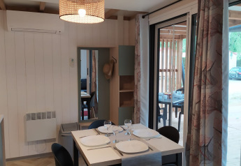 Interno di un alloggio glamping con tavolo apparecchiato, vetrate scorrevoli e vista sulla terrazza.