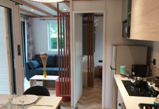 Moderne glampingbolig med fuldt udstyret køkken, spisebord og hyggelig stue i naturlige omgivelser.