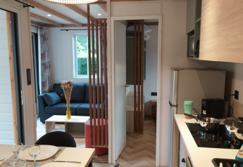 Alloggio glamping moderno con cucina attrezzata, zona pranzo e salotto accogliente in ambiente naturale.