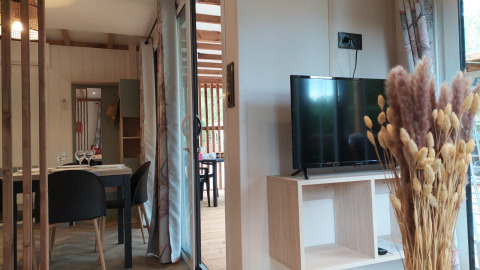 Alojamiento glamping luminoso con mesa de comedor, televisor, muebles de madera y flores secas.