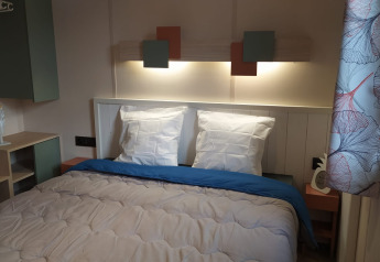 Camera glamping moderna con letto matrimoniale, luci a parete soffuse e tende con motivi eleganti.