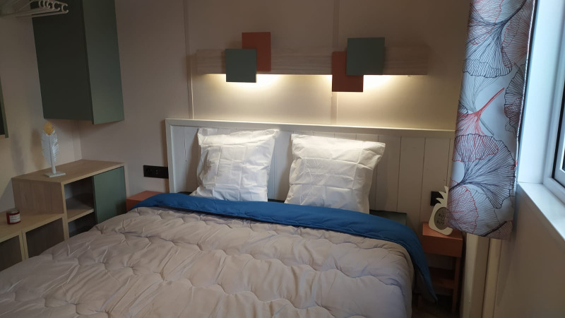 Dormitorio moderno de glamping con cama doble, luces de pared cálidas y cortinas con estampado elegante.