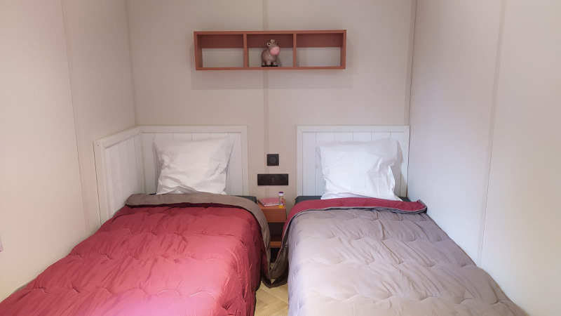 Dos camas individuales con edredones de diferentes colores en una habitación de glamping, estante en la pared.