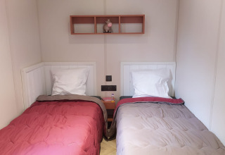 To enkeltsenge med forskelligt sengetøj i et glampingrum, med reol og pynt på væggen over natbordet.