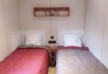 Due letti singoli con piumoni di colore diverso in una camera glamping, mensola a muro e comodino tra i letti.