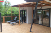 Terraza de madera con tumbonas frente al Chalet Tribu Premium en Flower Camping La Rivière, Francia.