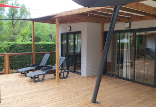 Terraza de madera con tumbonas frente al Chalet Tribu Premium en Flower Camping La Rivière, Francia.