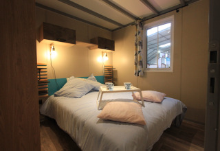 Slaapkamer in het Chalet Tribu Premium bij Flower Camping La Rivière, met dubbel bed en ontbijtplankje.