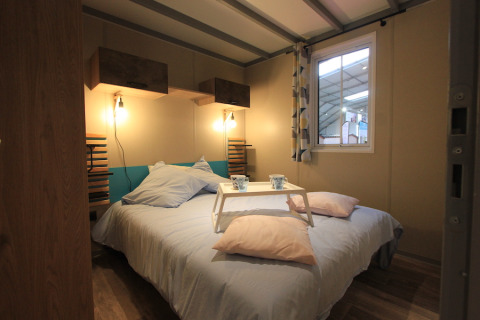 Schlafzimmer im Chalet Tribu Premium bei Flower Camping La Rivière, mit Doppelbett und Frühstückstablett.