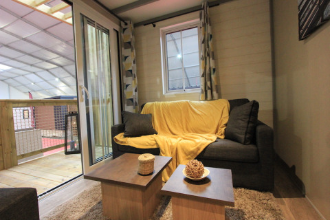 Stue i Chalet Tribu Premium, Flower Camping La Rivière, Frankrig med sofa, sofabord og udendørs altan.