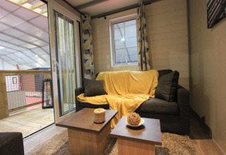 Stue i Chalet Tribu Premium, Flower Camping La Rivière, Frankrig med sofa, sofabord og udendørs altan.