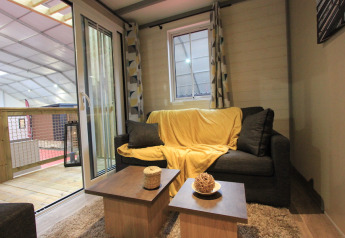 Wohnzimmer im Chalet Tribu Premium, Flower Camping La Rivière, Frankreich, mit Sofa und Balkon.